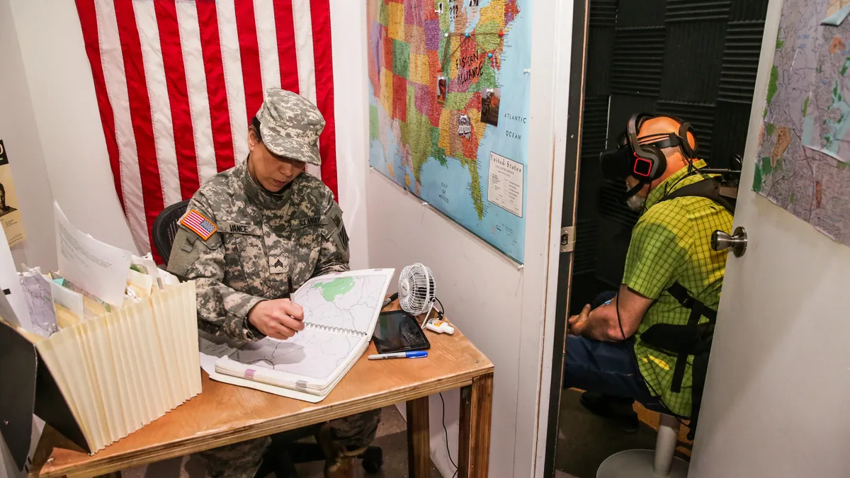 Inside the 2nd Civil War VR experience: an actor in military fatigues sits at a desk studying maps in a room decorated with an American flag and a large map of the United States, while a visitor in a VR headset views the experience in an adjacent space.