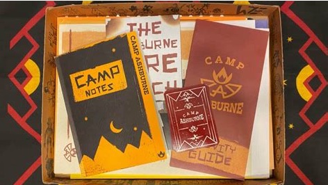 Contents of the Hunt A Killer: Camp Calamity box spread on a patterned surface, including a black 'Camp Notes' booklet, a dark red 'Camp Ashburne' welcome guide, and a 'Camp Activity Guide' booklet with a flame logo, all with hand-crafted, illustrated styling.